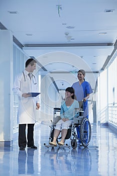 Smiling female nurse pushing and assisting patient in a wheelchair in the hospital, talking to doctor