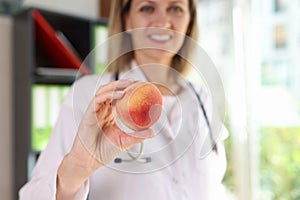 Smiling female nutritionist holds fresh peach fruit in her hand close-up.
