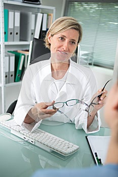 smiling female optician offering glasses frames to customer