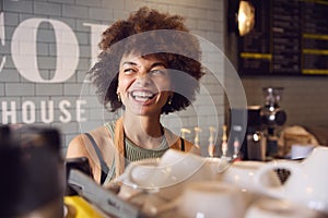 Smiling Female Owner Or Staff Serving Behind Counter In Coffee Shop