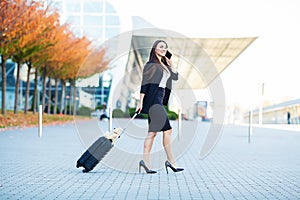 Smiling female passenger proceeding to exit gate pulling suitcase through airport concourse