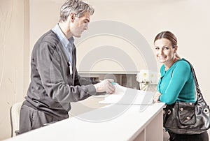 Smiling female patient in 40s received by male doctor at hospital reception desk
