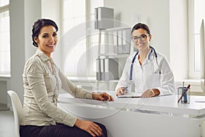 Smiling female patient at consultation with woman doctor sitting at table in office clinic.