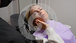 Smiling female patient with with dental problem talking with unrecognizable dental doctor during checkup and