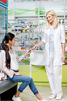 smiling female pharmacist giving pills to pregnant woman