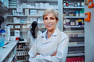 Smiling female pharmacist standing with cross arms in pharmacy drug store