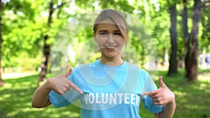 Smiling female pointing at volunteer word on t-shirt, forest conservation, earth