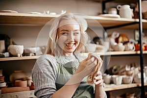 Smiling female potter in the workshop against rack of pottery