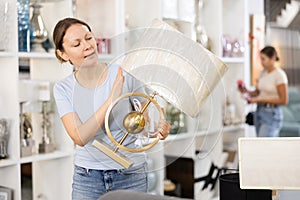 Smiling female purchaser choosing stylish table lamp in shop