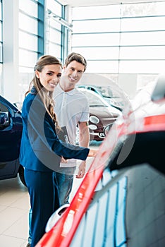 Smiling female sales manager showing red car to the