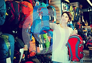 Smiling female shopper examining rucksacks in sports equipment s