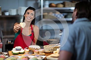 Smiling female staff giving heart shape cookie to customer at counter