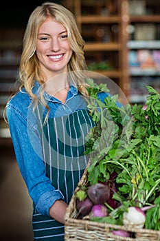 Smiling female staff holding a basket of fresh vegetables in organic section