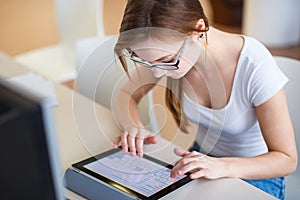 Smiling female student/ businesswoman using her tablet computer and a desktop computer