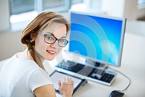 Smiling female student/ businesswoman using her tablet computer and a desktop computer