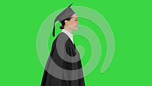 Smiling female student in graduation robe walking with her diploma on a Green Screen, Chroma Key.
