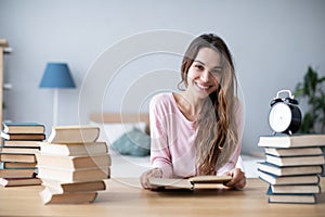 Smiling female student with a pile of books looks at the camera. Distance learning