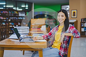 Smiling female student posing while working on laptop and searching for books to study, make report, find useful information in