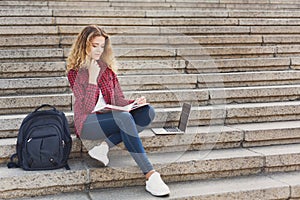 Smiling female student sitting on the stairs using laptop outdoo