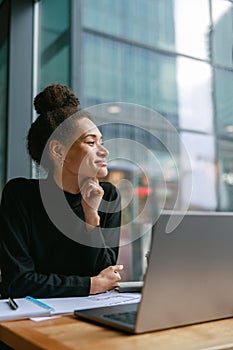 Smiling female student studying on laptop while sitting in cafe and looking at window