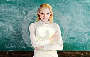 Smiling female teacher standing with teacher's journal in front of chalkboard. School teacher, lecturer with class