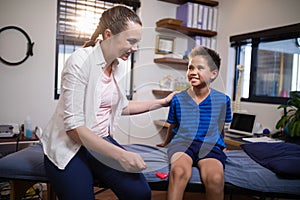 Smiling female therapist looking at boy while hitting at knee with reflex hammer