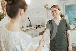 smiling female therapist in massage cabinet shaking hands