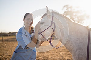 Smiling female vet stroking horse at barn