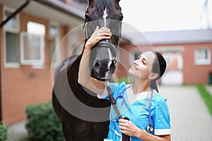 Smiling female veterinarian stroking black horse closeup