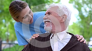 Smiling female volunteer comforting handicapped elderly man at hospital park
