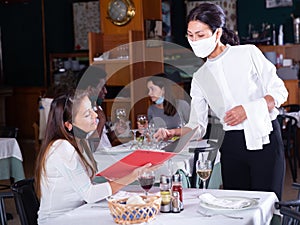 Smiling female waiter taking order from woman in restaurante diring virus