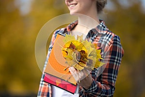 Smiling female young student outdoors holding yellow leaves