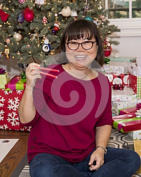Smiling fifty-eight year old Korean woman in front of a Christmas tree and presents