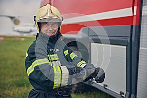 Smiling firefighter in yellow helmet and protective gloves standing in the outdoors