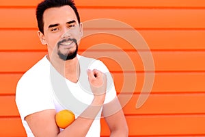 Smiling fit man holding bright orange on his bicep. Bright background. Copy space