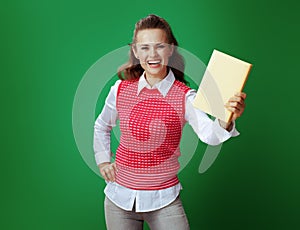 Smiling fit student showing yellow book on green background