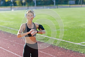 Smiling fit woman with headphones checking smartwatch on track field