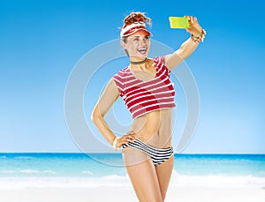 Smiling fit woman on seacoast taking selfie with mobile phone