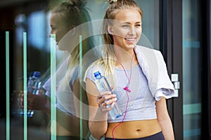 Smiling Fit Woman With Water Bottle Leaning Against Glass Wall