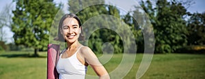 Smiling fitness girl with rubber mat, stands in park wearing uniform for workout and sport activities, does yoga