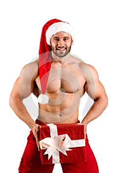 Smiling fitness white guy wearing Santa Claus hat with muscular body and big gift box, isolated