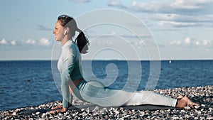 Smiling fitness woman slim body performing dog upward cobra posture exercising on sunset sunny beach