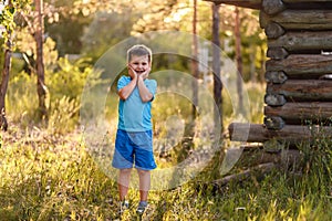 A smiling five-year-old boy in blue clothes stands tall in the Park on a natural background in the summer in the contra sunset