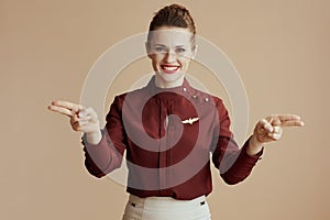 smiling flight attendant woman on beige showing where exits are