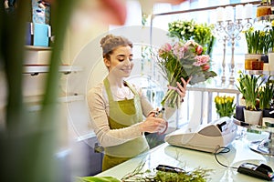 Smiling florist woman making bunch at flower shop