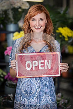 Smiling florists holding open sign placard in flower shop