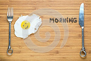 Smiling fried egg lying on a wooden cutting board with morning inscription near it. Classic Breakfast concept.