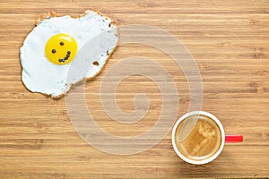 Smiling fried egg lying on a wooden cutting board with small red cup of coffee near it. Classic Breakfast concept.