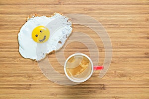 Smiling fried egg lying on a wooden cutting board with small red cup of coffee near it. Classic Breakfast concept.