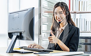 Smiling friendly asian female call-center agent with headset showing thumbs up for working on support hotline in the office,